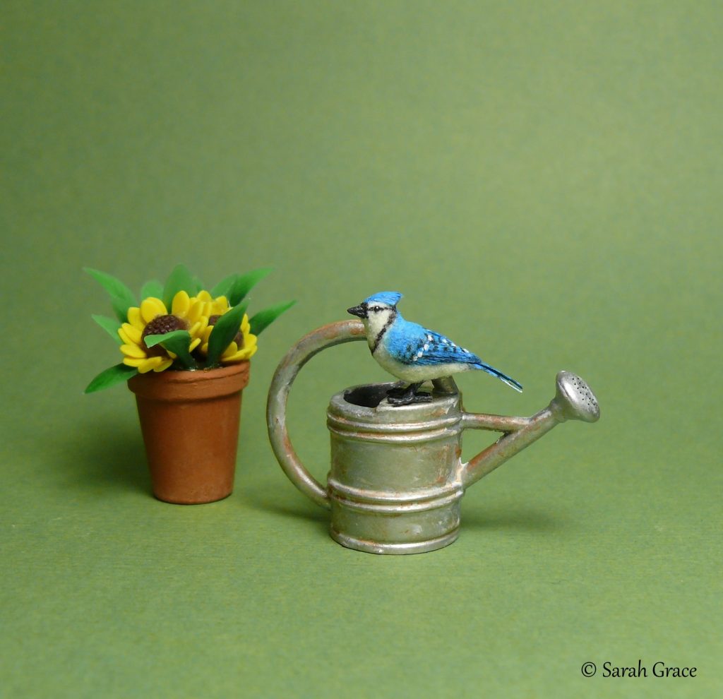 Handmade miniature blue jay bird sculpture perched on a watering can with bold blue feathers and crest by Sarah Grace