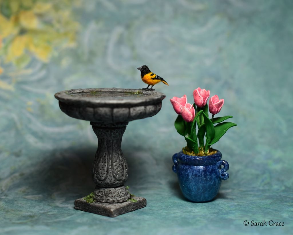 Realistic miniature Baltimore oriole bird sculpture featuring vivid orange plumage by Sarah Grace