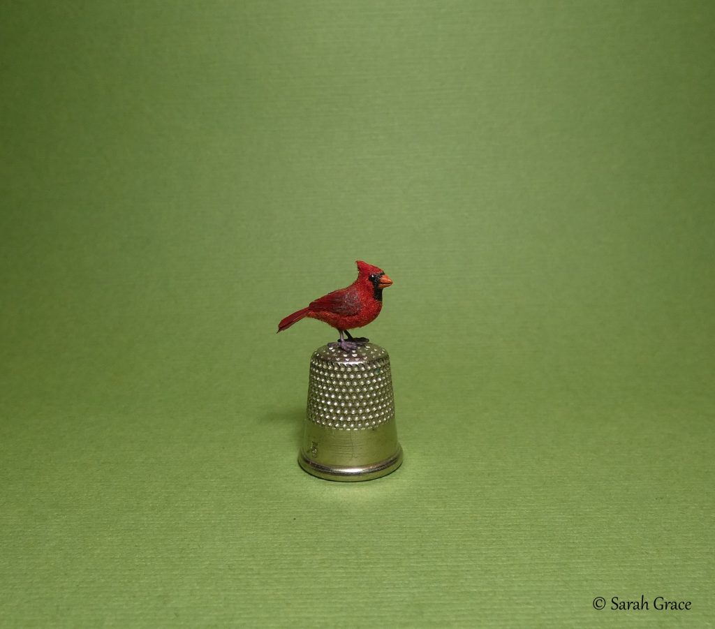 Realistic miniature northern cardinal bird sculpture with bright red plumage and black mask details by Sarah Grace