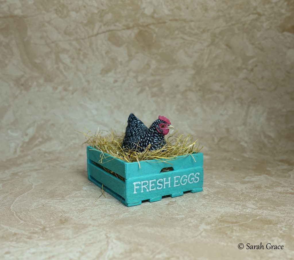 Charming 1:12 scale miniature Plymouth Rock hen sculpture perched in a wooden crate with intricate feather detailing by Sarah Grace