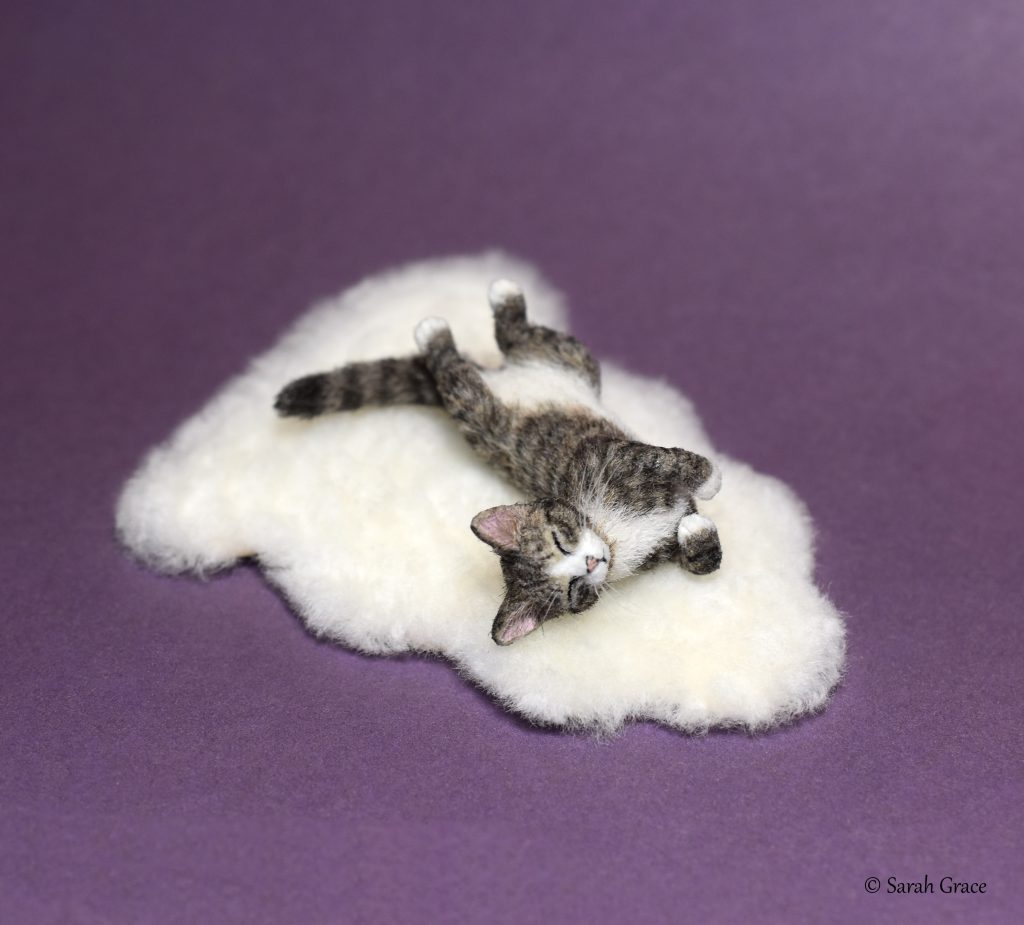 Realistic miniature sculpture of a sleepy kitty cat curled up in a relaxed resting pose with soft fur details by Sarah Grace